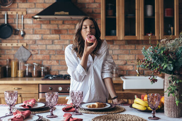 Young woman eating a donut with pleasure in the kitchen
