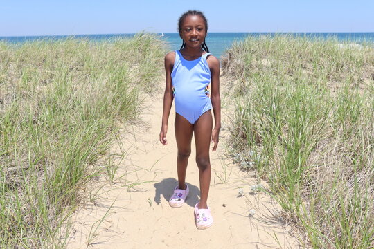 Young black child wearing swiming bathing suit walking down sand pathway on beach ocean background outdoors sunny day on marthas vineyard island