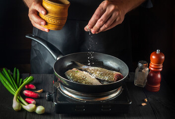 Chef prepares fresh fish in pan sprinkling salt with the ingredients. Preparing to cook fish food. Working environment in the restaurant kitchen