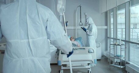 Doctor and nurse in ppe overall treating aged woman patient with covid-19 in hospital ward - Powered by Adobe