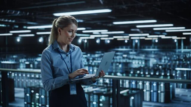 Portrait of IT Specialist Using Laptop in Data Center. Big Server Farm Cloud Computing Facility with Female System Administrator Monitoring. Cyber Security, Network Protection Services. Medium Wide