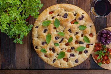 round focaccia with basil, black olives and tomatoes on wooden background