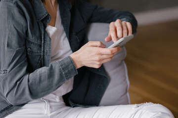 top view, European woman in a gray shirt and white jeans sitting in a chair and chatting on the phone, texting, internet surfing or online shopping, online shopping. caucasian woman ordering food
