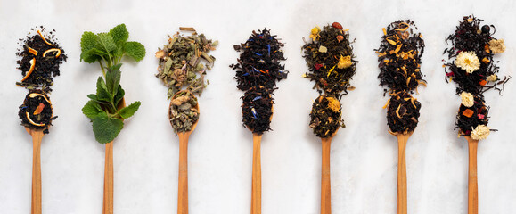 Large assortment of dry tea in spoons from herbs, flowers, berries and fruits on on  stone marble...