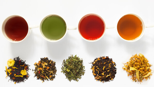 Four cups of tea  on white   table with large assortment of herbal, flower, berry and leaf dry teas.