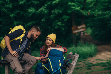 Obraz premium Hikers sitting on a bench in the forest and making a break while using a smartphone