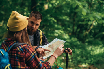 Couple of hikers using trekking poles and map while spending the day in nature