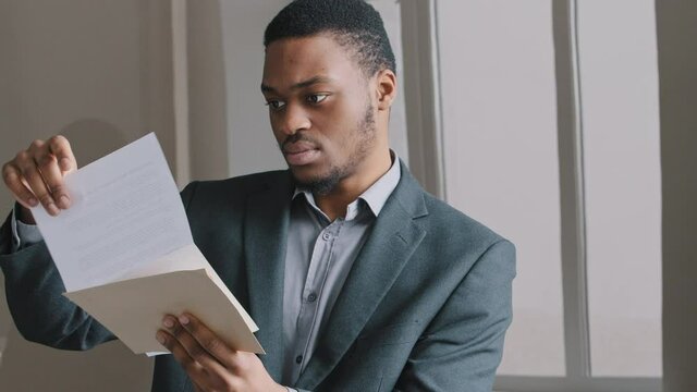 Focused young 25s African ethnicity man holding paper document in hands, feeling unhappy stressed exam failure, banking loan money debt notification, negative news in correspondence, eviction notice