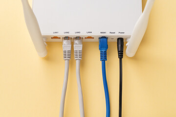 White Wi-Fi wireless router with connected network and power cables on a yellow background. Home and office wlan router with inserted internet cables. Internet hardware close-up.