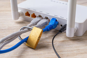 Locked padlock on network cables connected to white Wi-Fi wireless router on a desk. Prohibit and...