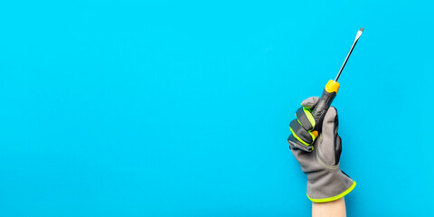 Screwdriver. Yellow and black screwdriver in the hand of an electrician on a blue monochrome background. Repair and installation tool. Banner for the design and printing of construction topics.