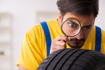 Young male garage worker with tyre at workshop