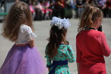 Three little girls with long hair with a bow on their head in beautiful dresses in the hands of a...