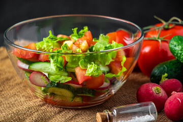 Fresh vegetable salad in a glass bowl on dark background. Vegan organic food, seasonal summer dish.