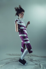 Creative stylish woman with curly fluffy hair in purple dress with white stripes