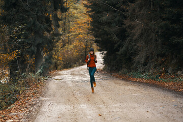 Obraz premium happy travel with a backpack in a warm sweater, trousers and boots walks along the road in the autumn forest