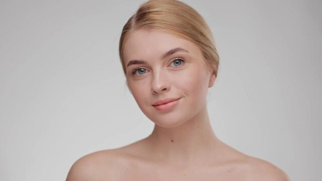 Skin care concept. Beauty face. Smiling young woman look at the camera. Healthy skin portrait natural beauty girl on light background at studio. Slow motion. Caucasian blonde female with grey eyes.