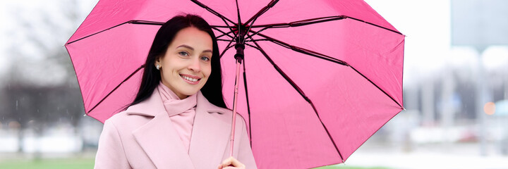 Portrait of woman in coat who stands in rain and holds pink umbrella
