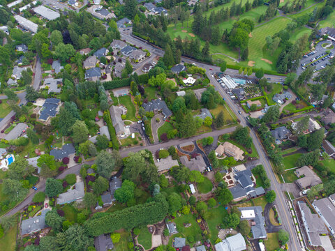 The photo shows a suburban landscape. We see rooftops, a lot of greenery, and many highways. In the right corner of the photo you can see a large green meadow. Aerial photography.
