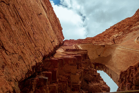 A view from below of a cloudy sky, from inside an old abandoned church. A ruined part of a brick wall with a window.