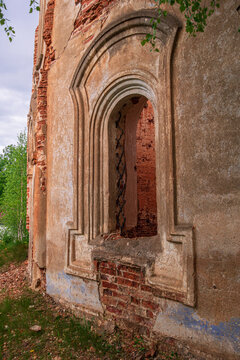 Close-up: a window with the remains of a lattice. An old abandoned church. In the background, a forest and a cloudy sky.