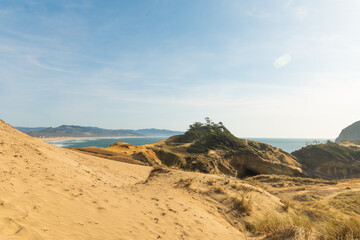 In the photo we see the sandy hilly coast of the ocean. In the background you can see the edge of the ocean, mountains. Desert area. No greenery. No people. Place for your insert.
