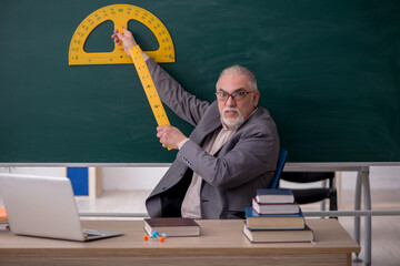 Old male teacher holding line in front of blackboard