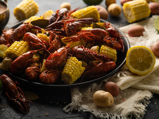 A beautiful still life of boiled crayfish, pieces of boiled corn, lemon, many vegetables. White napkin, dark background. Careful viewing. Close-up.There are no people in the photo. Bright colors.