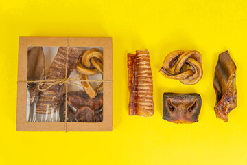 Kit of dried meat treats for training and encouraging dogs. Contents of box are placed next to the packaging for clarity, top view, yellow background, copy space.