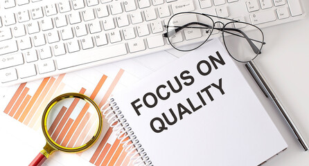 Focus on Quality text written on a notebook with keyboard, chart,and glasses