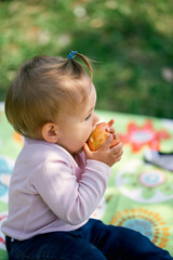 Little girl sits on a blanket and bites an apple. Close-up. Side view
