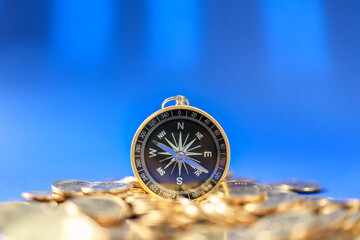Business, Money Direction and Planning Concept. Closeup of vintage compass on pile of gold coins with blue background. - obrazy, fototapety, plakaty