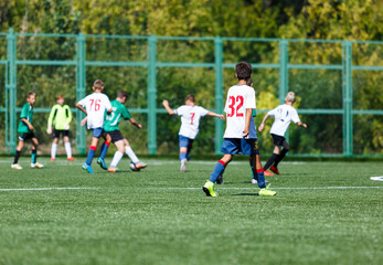 Boys in green sportswear running on pitch.  Young footballers dribble and kick football ball in game. Training, active lifestyle, sport 