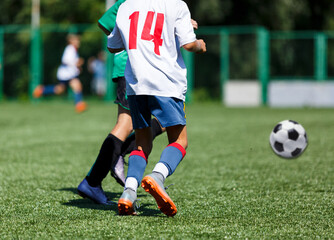 Fototapeta premium Boys in green sportswear running on pitch. Young footballers dribble and kick football ball in game. Training, active lifestyle, sport 