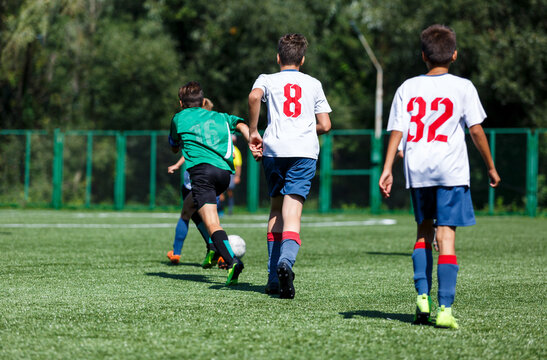 Boys in green sportswear running on pitch.  Young footballers dribble and kick football ball in game. Training, active lifestyle, sport 