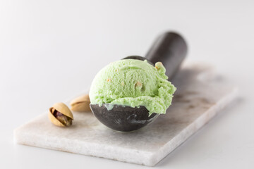 Pistachio ice cream in a scoop on a small marble slab 