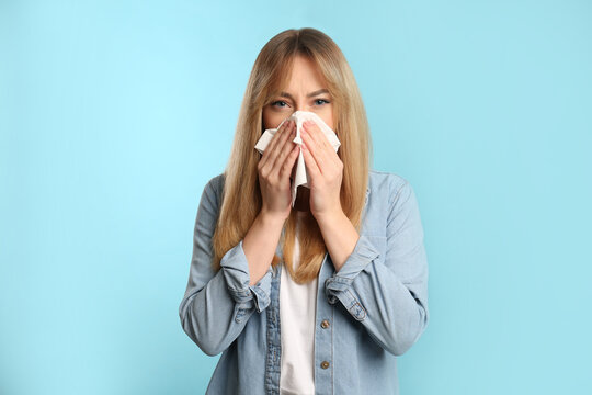 Young woman with tissue suffering from runny nose on light blue background
