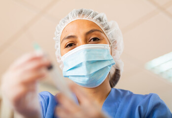 Female nurse or doctor wearing in face mask and medical uniform holding vial and syringe