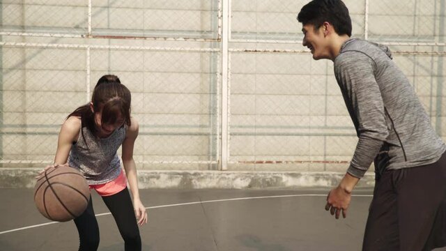 young asian couple playing basketball for fun on outdoor court