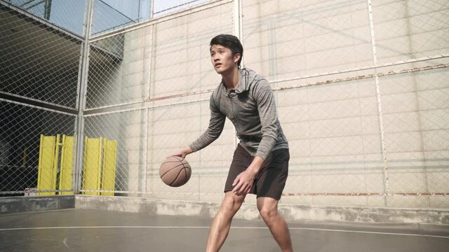 young asian basketball player practicing dribbling skills alone on outdoor court