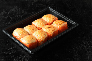 A set of rolls with red fine-grained tobiko flying fish caviar in a delivery box on a black wooden background.