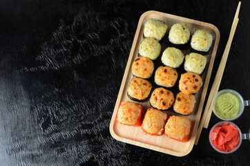 A set of various rolls with chopsticks in a wooden bamboo plate on a black wooden background with ginger and wasabi