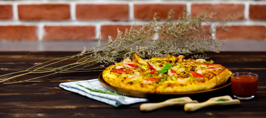 Close up side view of yummy seafood pizza served on brown table near brick wall with seasoning, glass of ketchup, napery, and luxury decorated by dried flower to be high class of Italian meal