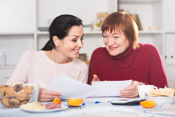 Happy women with documents sitting at table in home interior