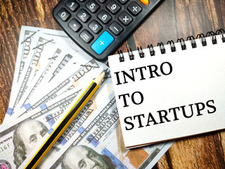 Fototapeta premium Business concept.Text Intro to startups with banknote,pencil and calculator on wooden table background.