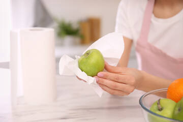 Woman wiping green apple with paper towel in kitchen, closeup