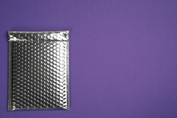 Padded envelope with bubble wrap on purple background, top view. Space for text