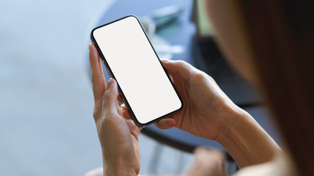 Over shoulder close up view of female hand holding smartphone with mock-up screen