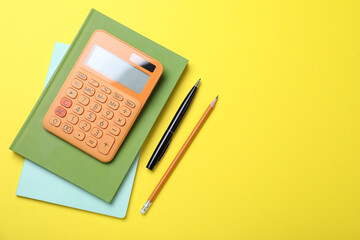 Calculator, notebooks, pen and pencil on yellow background, flat lay. Space for text