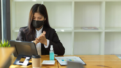 Businesswoman with medical mask hands sanitising with alcohol gel before start doing work